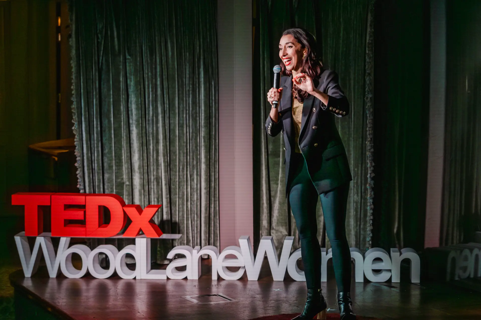 Raja Skogland speaking on the TEDx WoodLane Women stage in London, red TEDx letters beside her